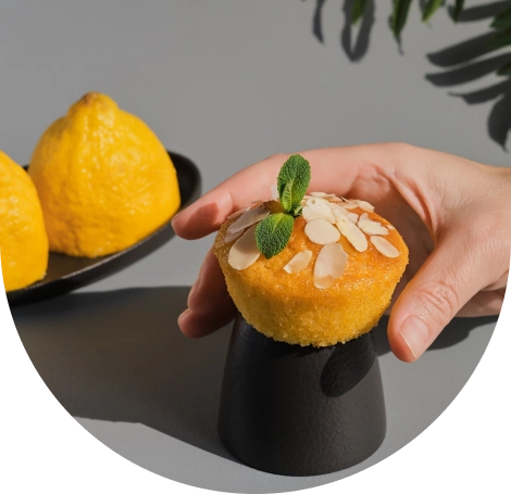Elegáns citromos minitorta desszert, mandulaforgáccsal és friss mentalevelekkel díszítve, modern fekete tálcán tálalva, háttérben egész citromokkal.
