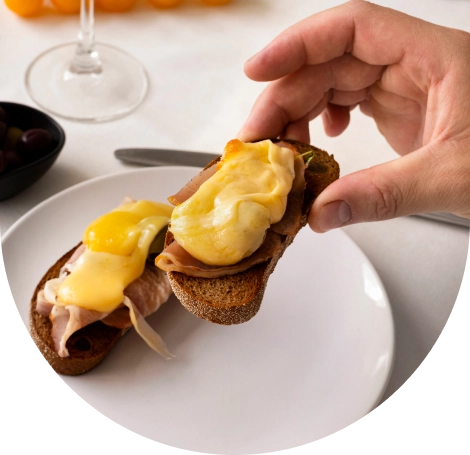 Közelkép egy ínyenc pirítósról sonkával és krémes Benedict-mártással, amelyet fehér tányéron tálalnak egy elegáns reggeli vagy brunch alkalmával.