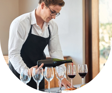 Egy profi sommelier kötényben vörösbort tölt elegáns poharakba egy fényűző étterem kifinomult belső terében, egy luxus étkezés során.